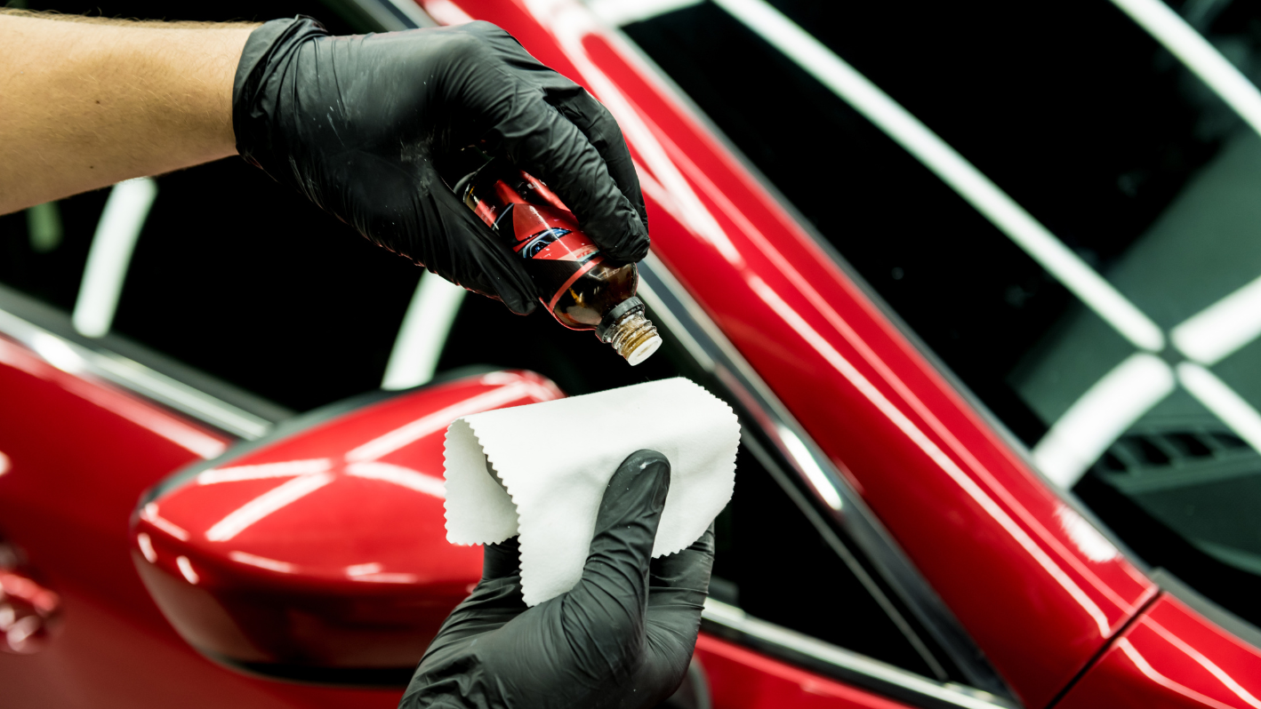 A person cleaning a red car with a cloth